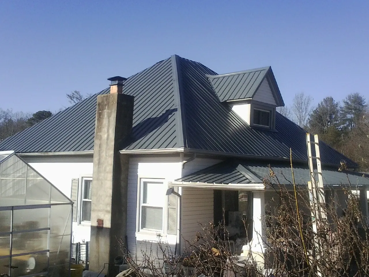 Dark blue standing seam metal roof on a white farmhouse with dormer — Slate & Tile Roof Repair by Roofing Brothers in Milanville