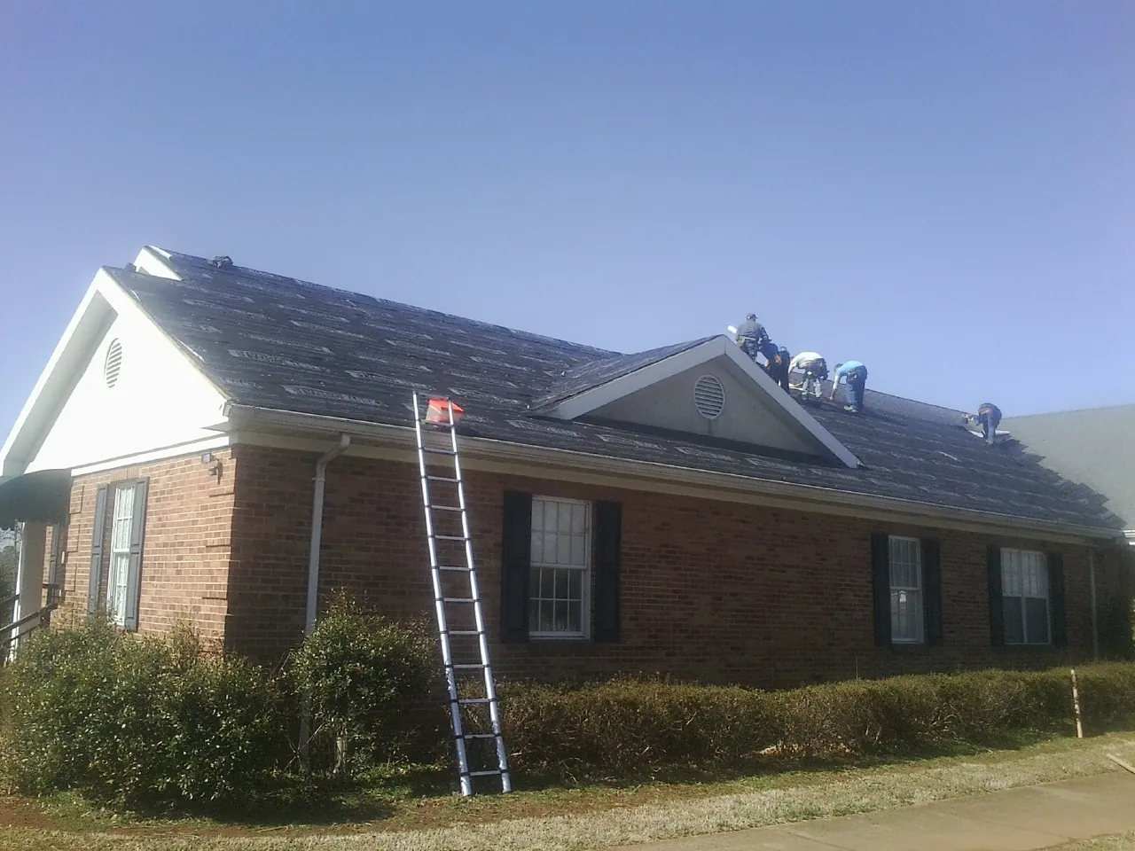 Crew tearing shingles off a brick ranch roof with a ladder set — Emergency Roof Repair work by our crew in Milanville