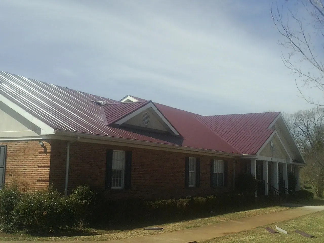 Red metal roof with gabled entries on a long brick building, from a Hail Damage Roof Repair job in Milanville