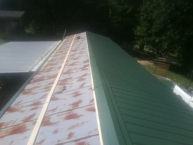 Old rusted panels beside newly installed green metal roofing — Wind Damage Roof Repair by Roofing Brothers in Milanville