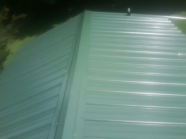 New green metal panels meeting at the ridge of a roof — Flat Roof Repair work by our crew in Milanville