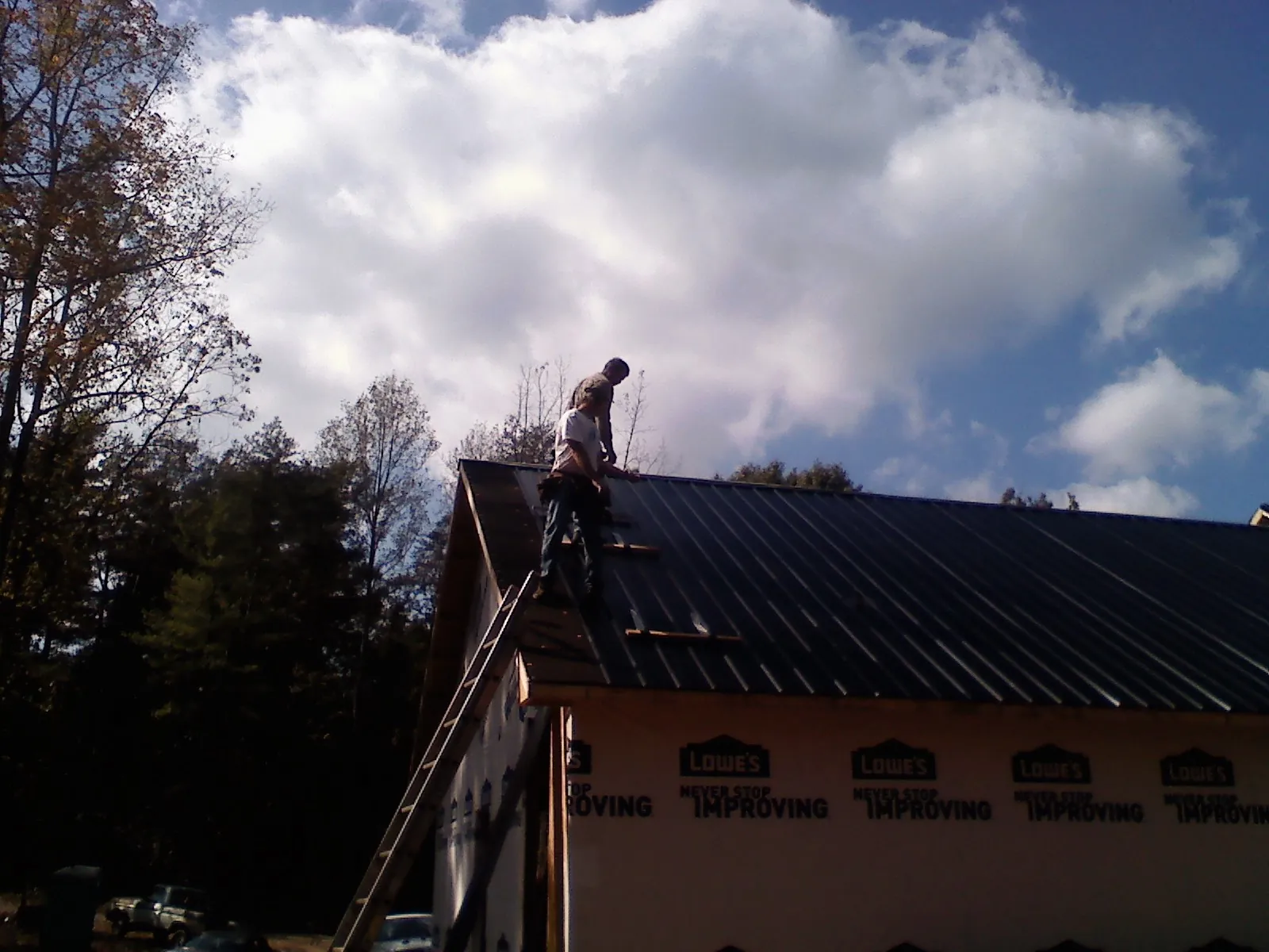 Roofer fastening dark metal panels high against a cloudy sky, from a Roof Inspection job in Milanville