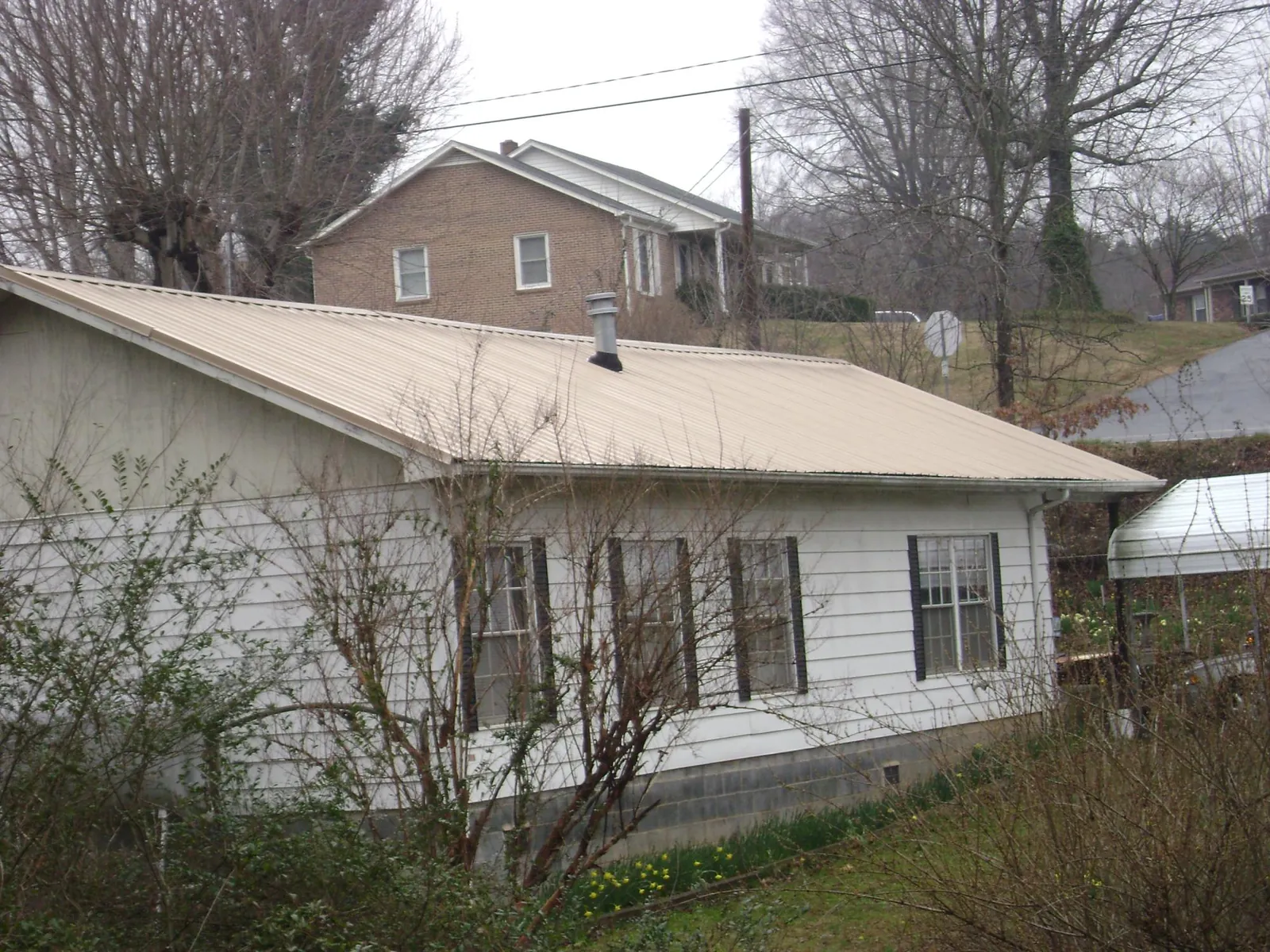 Tan metal roof on a white sided house set into a hillside — Commercial Roofing by Roofing Brothers in Milanville